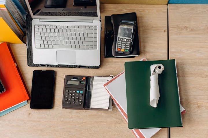 Bureau organisé avec ordinateur portable, calculatrice, terminal de paiement et documents, prêt pour une réunion de conseil.